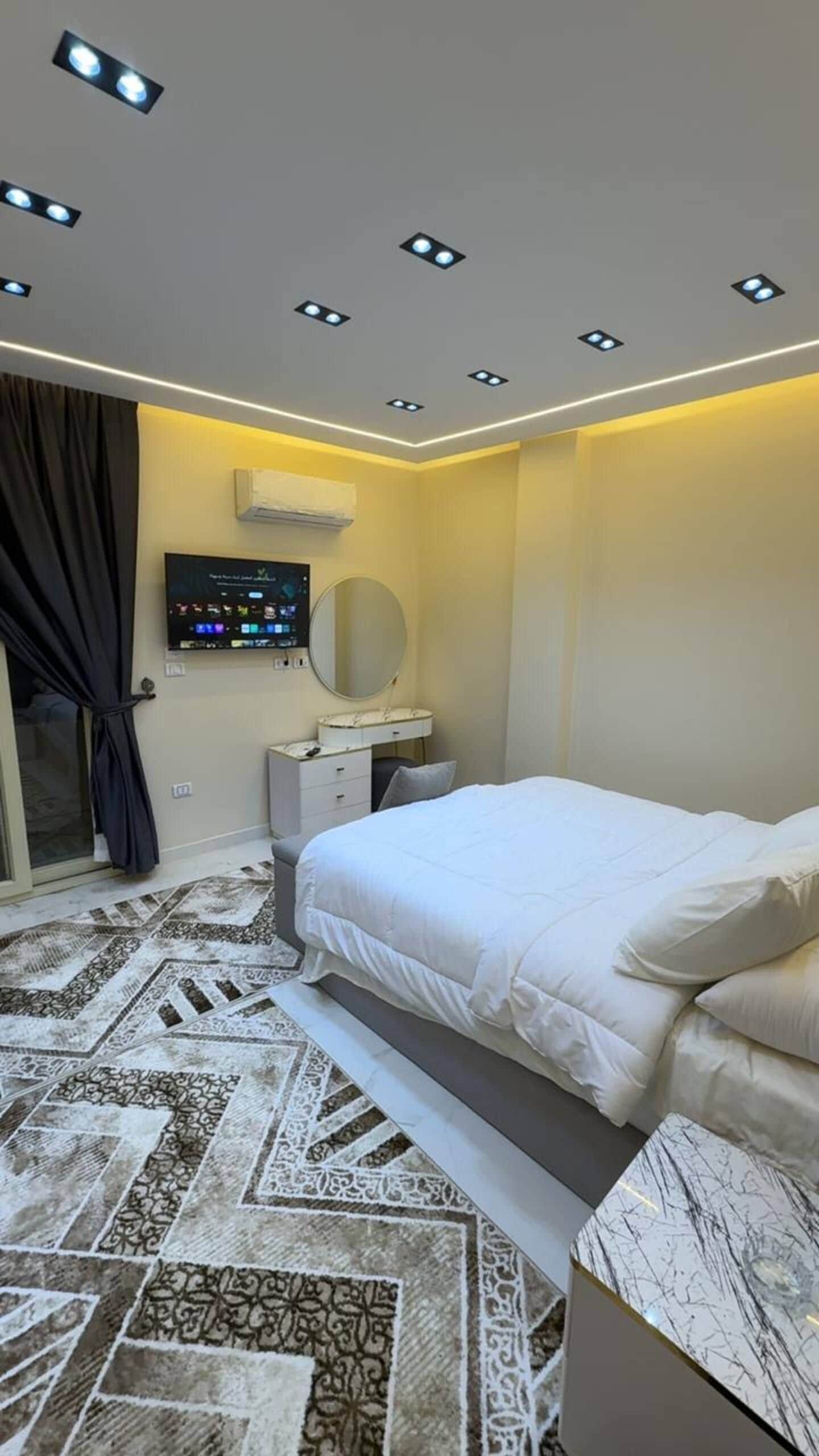 Une chambre à coucher moderne avec un lit, une table de chevet et un téléviseur fixé au mur.