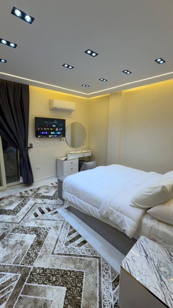 A modern bedroom with a bed, bedside table, and a television mounted on the wall. - Cozy 1-bedroom studio in tranquil Giza Governorate with AC (Giza Governorate)
