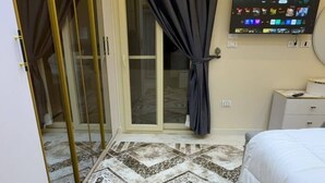 Habitación de hotel con cama, televisión, alfombra estampada y puerta corredera de vidrio.