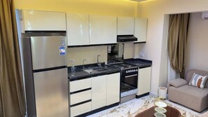 A compact kitchen with a refrigerator, stove, oven, and sink. There is a beige sofa and a small table with a lamp in the adjacent living area. - Cozy 1-bedroom studio in tranquil Giza Governorate with AC (Giza Governorate)