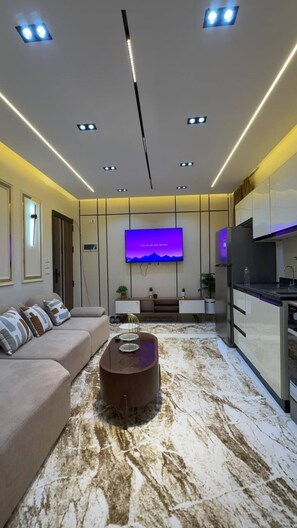A modern living room with a sofa, a coffee table, a flat-screen TV, and a kitchen area. - Cozy 1-bedroom studio in tranquil Giza Governorate with AC (Giza Governorate)