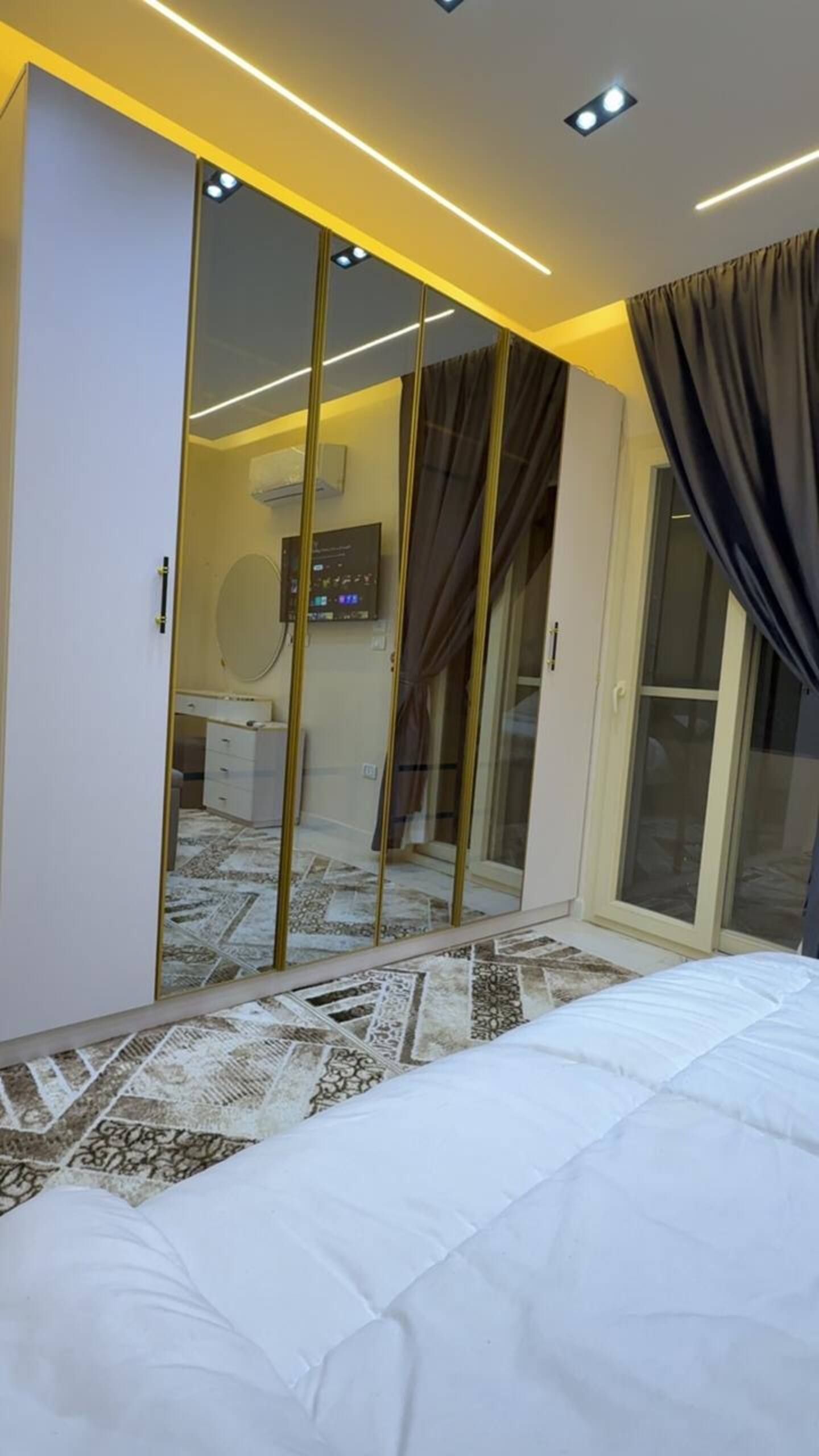 Un dormitorio con cama, armario con espejo, televisor y baño con ducha.