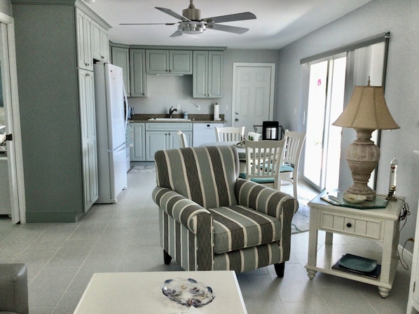 Amplia sala de estar con un sillón a rayas, comedor con sillas blancas y cocina con armarios azul claro.
