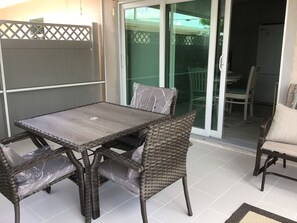 Un patio con mesa y sillas, un cerramiento de vidrio corredizo que da a un balcón y vistas al exterior.