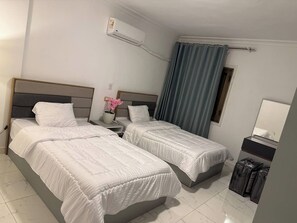 A hotel room with two beds, a bedside table with a lamp, a window with curtains, and a wall-mounted air conditioner. - Apartment in quiet neighborhood in Dokki (Giza Governorate)