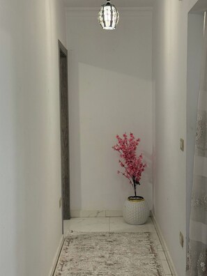 Een hal met een wit tapijt met textuur, een witte vaas met roze bloemen en een hanglamp.