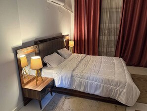Een opgemaakt bed met witte lakens, een houten hoofdbord en twee nachtlampjes met gele kapjes.