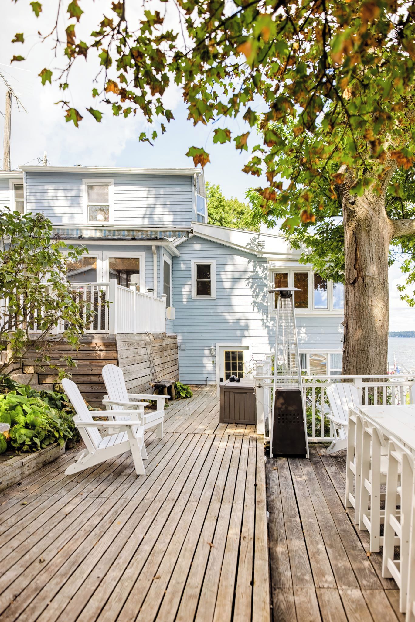 A wooden deck with white chairs, a small table, and a metal heater.