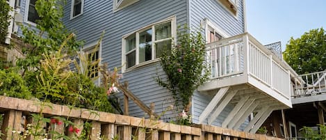 Une maison à deux étages, dotée d’un mur de soutènement en pierre et d’une terrasse en bois.
