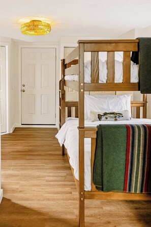 Une chambre avec un lit superposé, une tête de lit en bois, du linge de lit blanc et une couverture rayée aux couleurs vives.