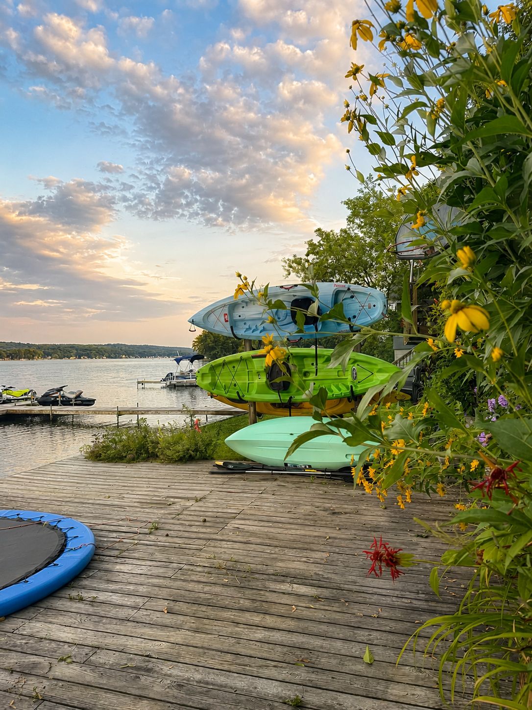 Eine Holzsteganlage mit Kajaks und einem Stand-Up-Paddle, mit Blick auf ein Gewässer.