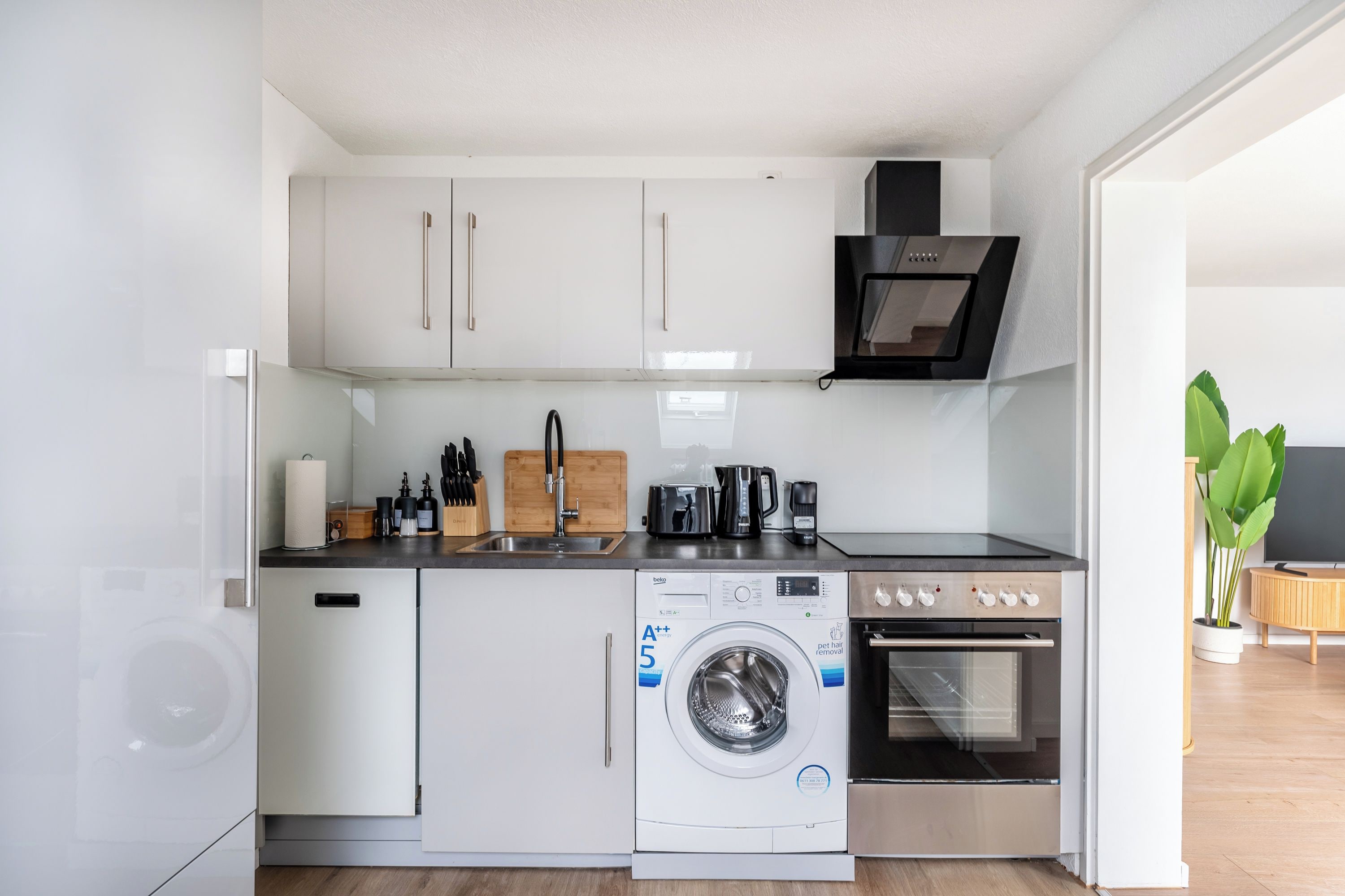 A compact kitchen with a washing machine, oven, and coffee maker.