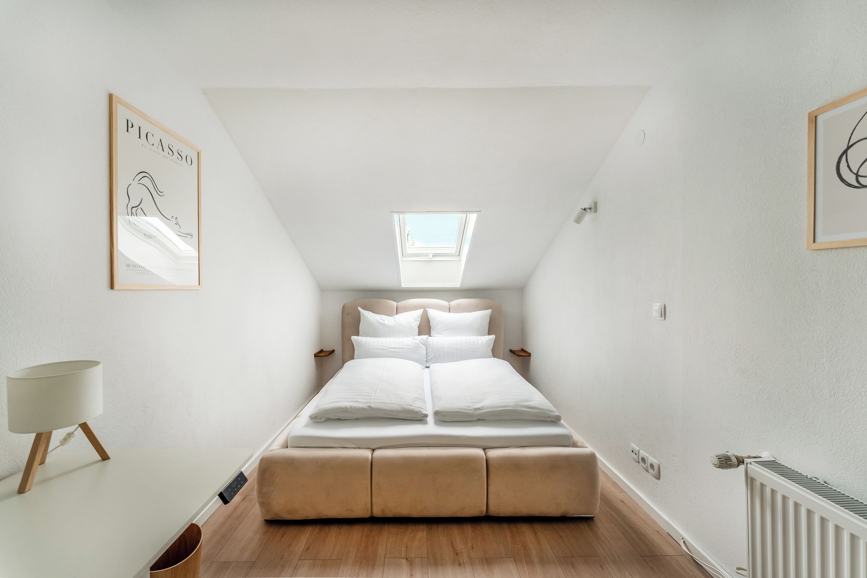 Une chambre à coucher avec un lit, une fenêtre, une table de chevet, une lampe et un radiateur.