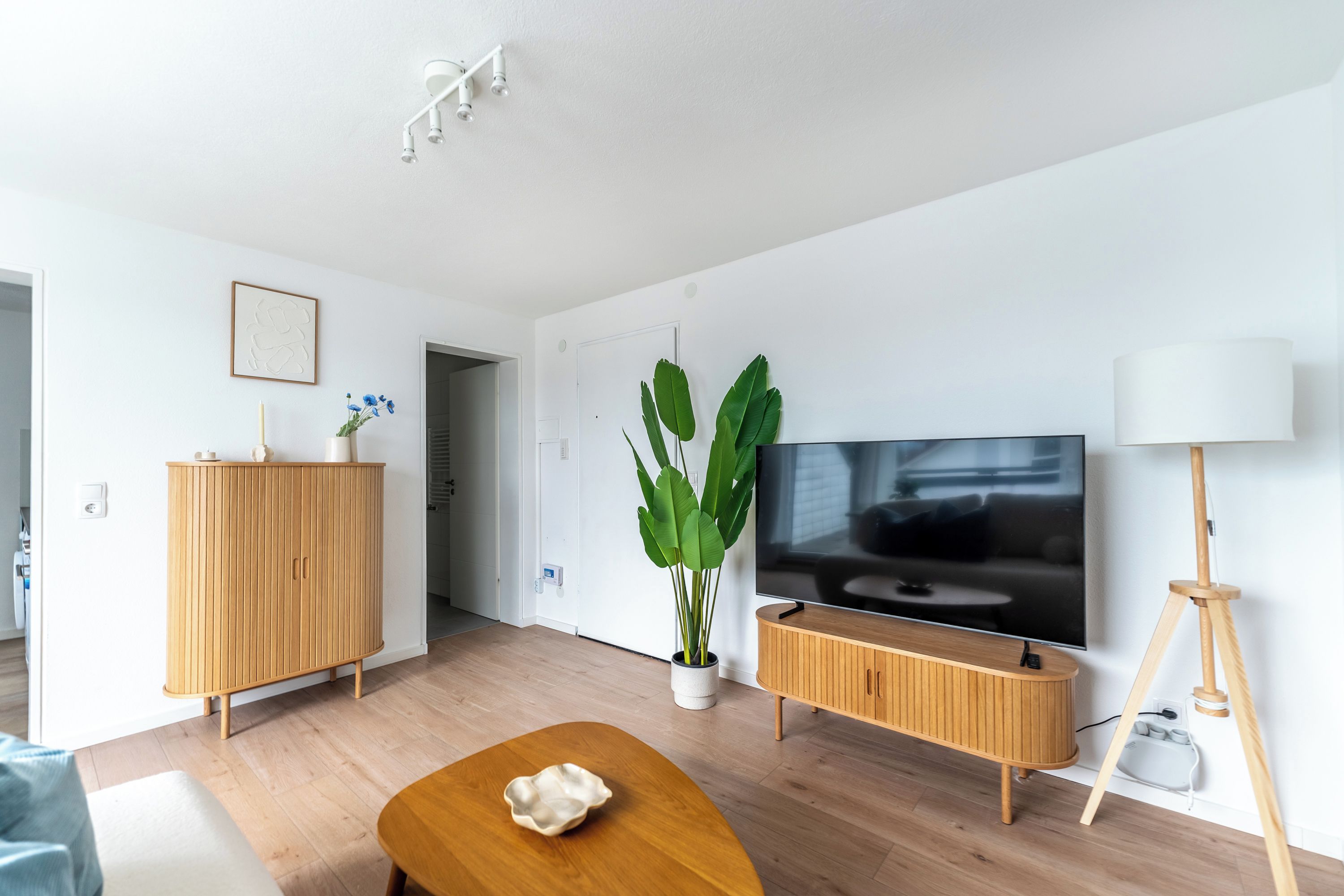Una sala de estar moderna con televisor de pantalla plana, muebles de madera, una planta en maceta y una lámpara de pie.