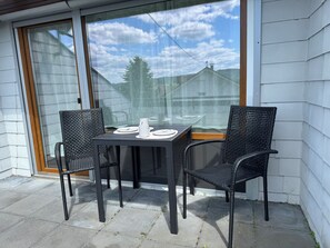 A patio with a table and two chairs, a sliding glass door, and a view of a residential area. - Bright rooftop serviced apartment near Zurich. Parking available and pet-friendly! (Küssaberg)
