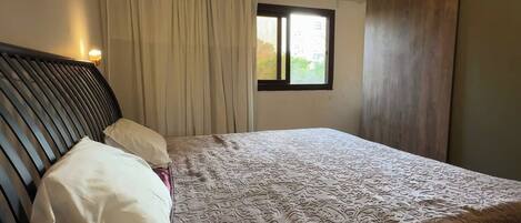 Un dormitorio con cama, ventana y cortinas.