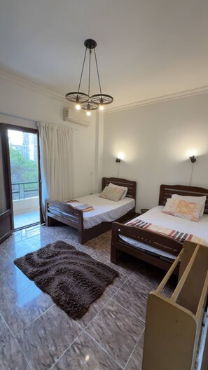 Habitación de hotel con dos camas, un tapete marrón, un candelabro en el techo y vistas al exterior.