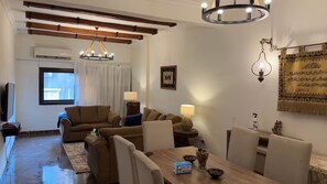 Ein Wohnzimmer mit einer Sofagarnitur, einem Esstisch mit Stühlen, einer Chandelier und einem Wandbild.