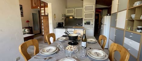 A dining area with a table set for six, wooden chairs, a chandelier, and a kitchen in the background.
