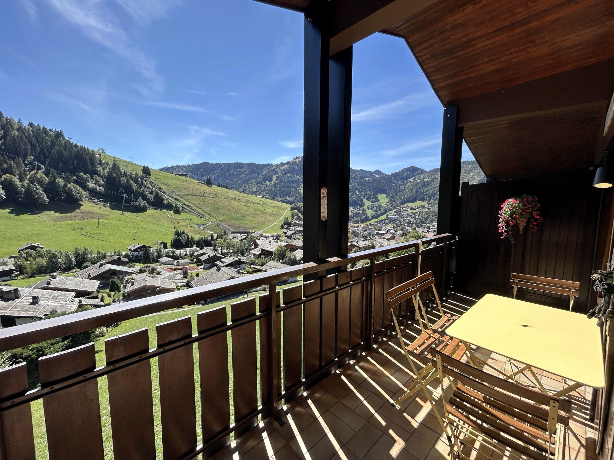 En balkon med gelænder i træ, et gult bord og en bænk.