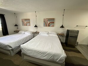 Ett hotellrum med två separata sängar, ett kylskåp, sängbord, lampor och abstrakt konst på väggen.