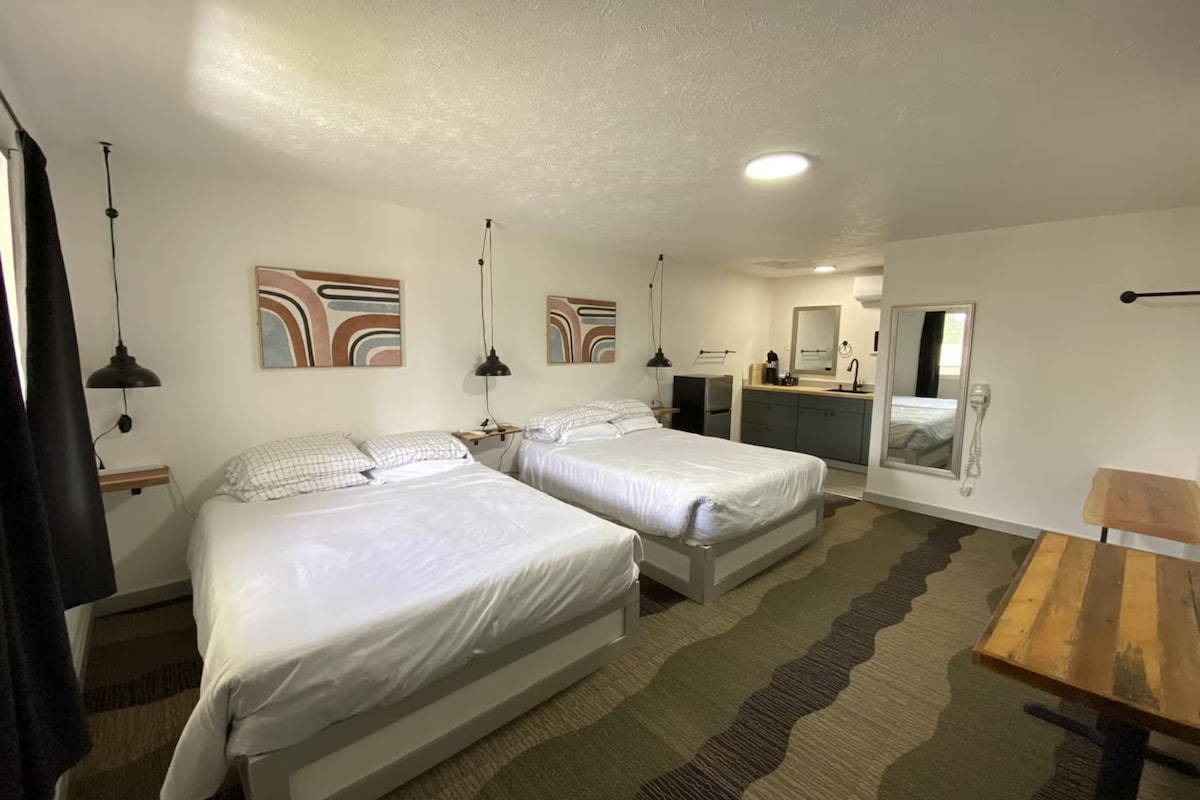 Ett hotellrum med två sängar, ett skrivbord, en spegel och konstverk på väggarna.