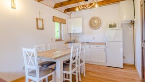 Une cuisine avec des meubles blancs, une table en bois et des chaises. Il y a une horloge au mur et une fenêtre avec un rideau.