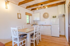 A kitchen with white cabinets, a wooden table, and chairs. There is a clock on the wall and a window with a curtain. - Domki Za Wydmami (Mrzeżyno)