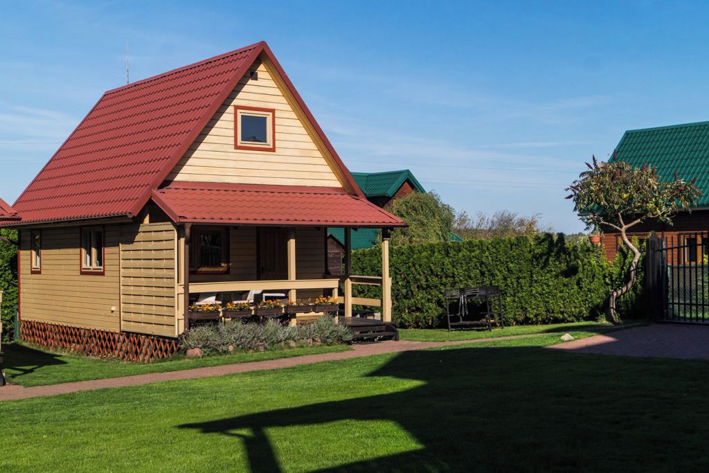A single-story wooden house with a red roof, a front porch, and a small window.