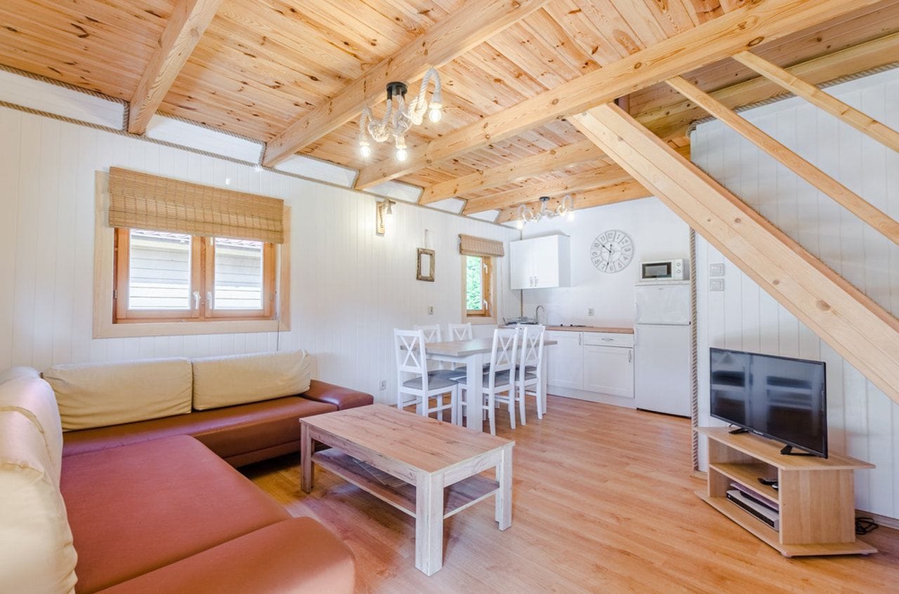 Hyggelig indretning med træloft, sofa, spisebord, fjernsyn og et køkkenområde.