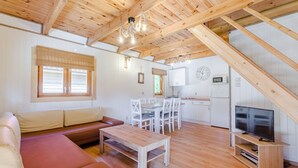 Un intérieur chaleureux avec un plafond en bois, un canapé, une table à manger, un téléviseur et un coin cuisine.