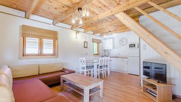 Hyggelig indretning med træloft, sofa, spisebord, fjernsyn og et køkkenområde.