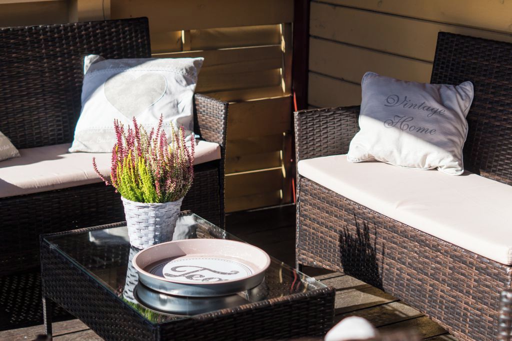 A wicker sofa with cushions, a glass table with a tray, and a potted plant.