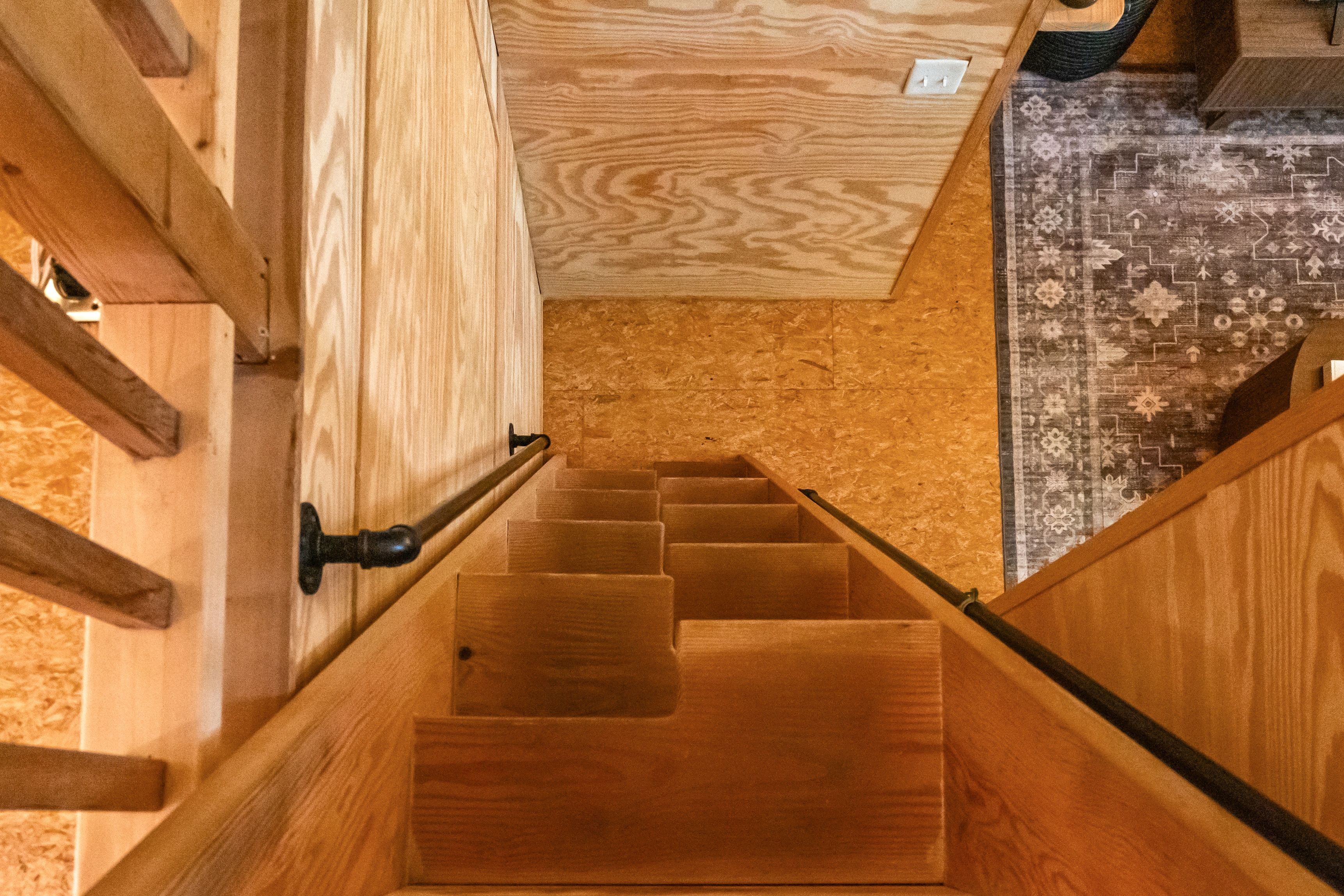 Una escalera de madera con barandilla que conduce a una habitación con alfombra estampada y suelo de madera.