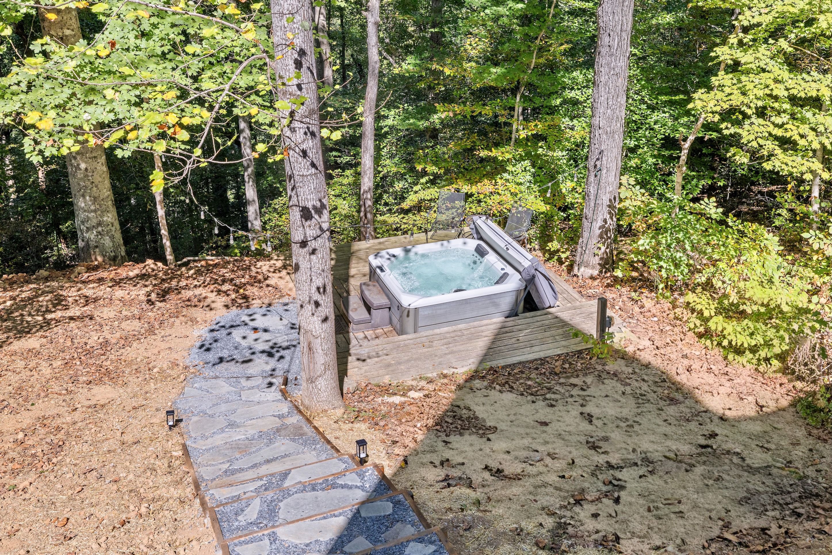 A hot tub surrounded by a wooden deck and stone pathway, set in a wooded area.