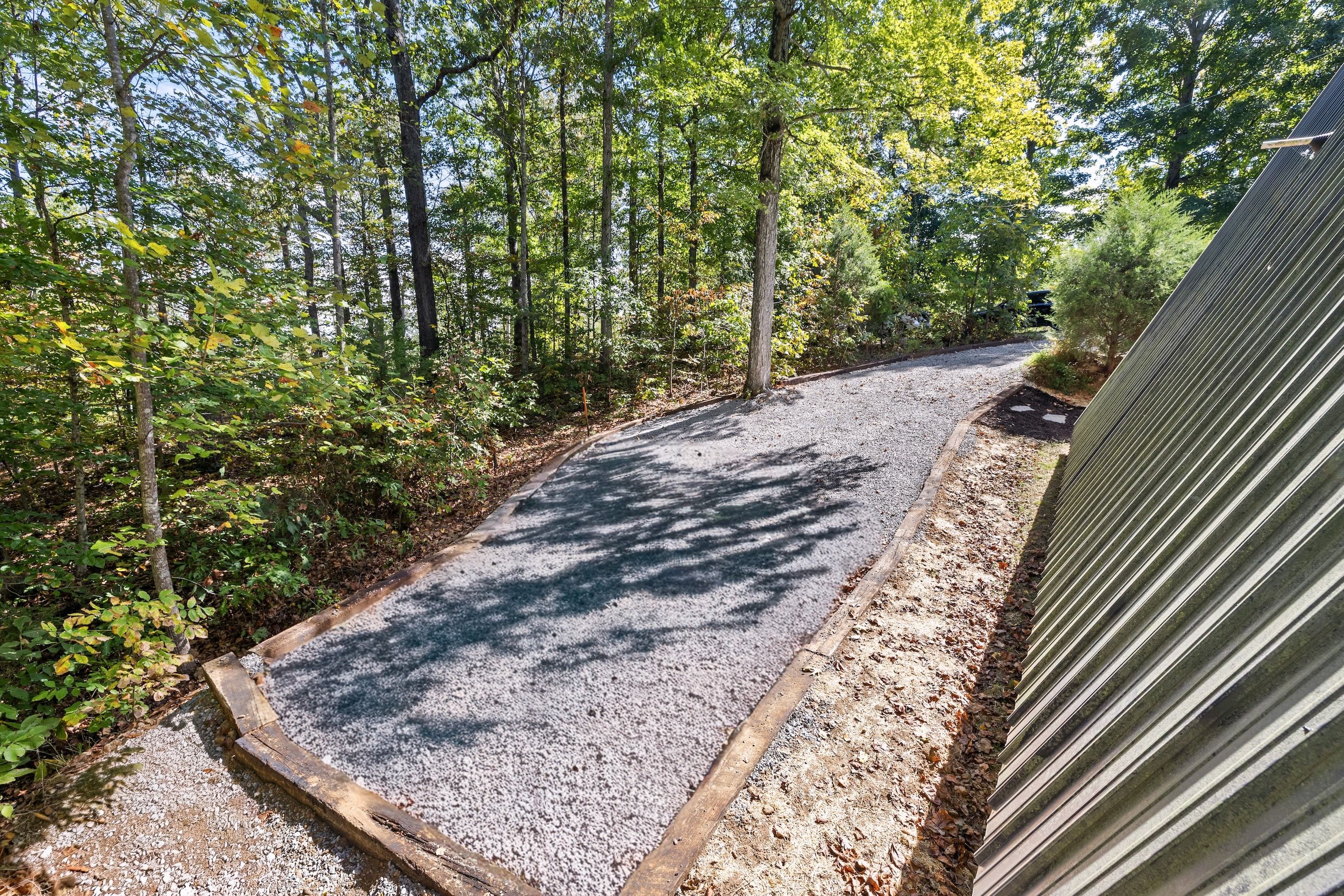 A gravel path in a wooded area with trees and a metal structure on the right.