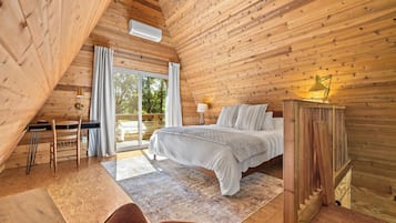 A bedroom with a bed, a desk, a chair, a lamp, and a view of the outdoors.