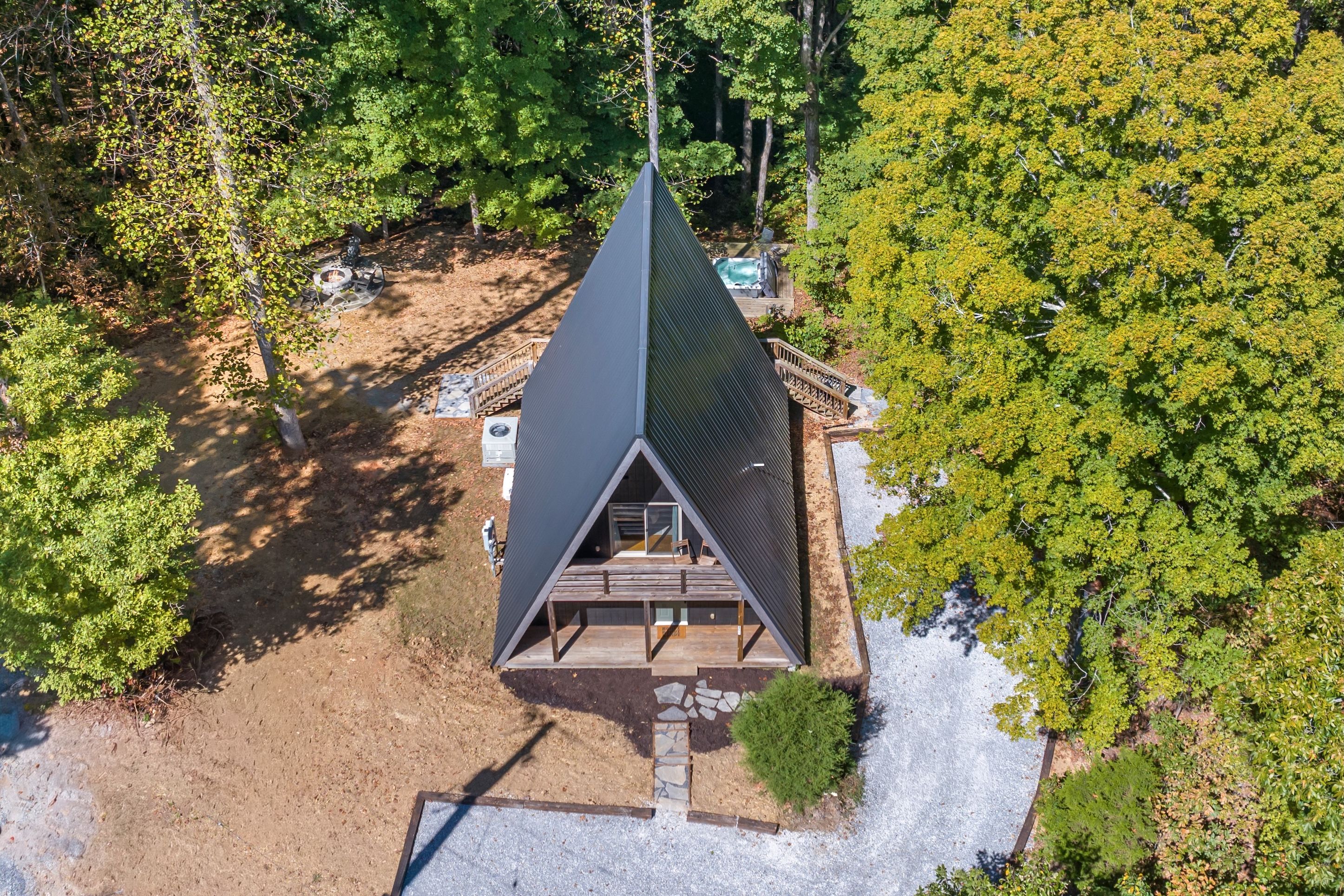 A triangular-roofed cabin with a deck, surrounded by trees.