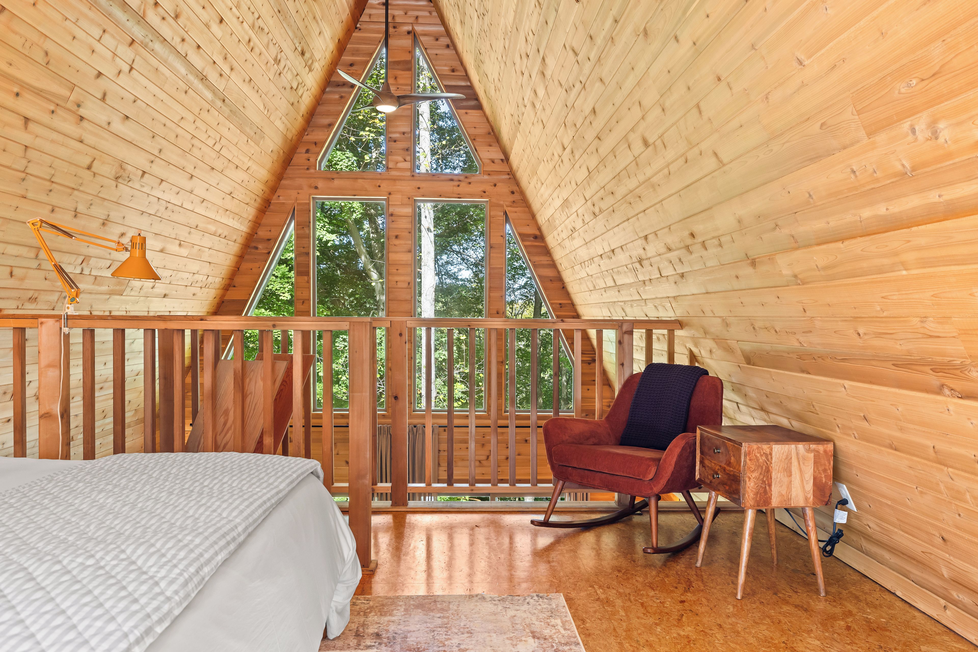 Un interior de madera con una cama, un sillón mecedor y un escritorio.