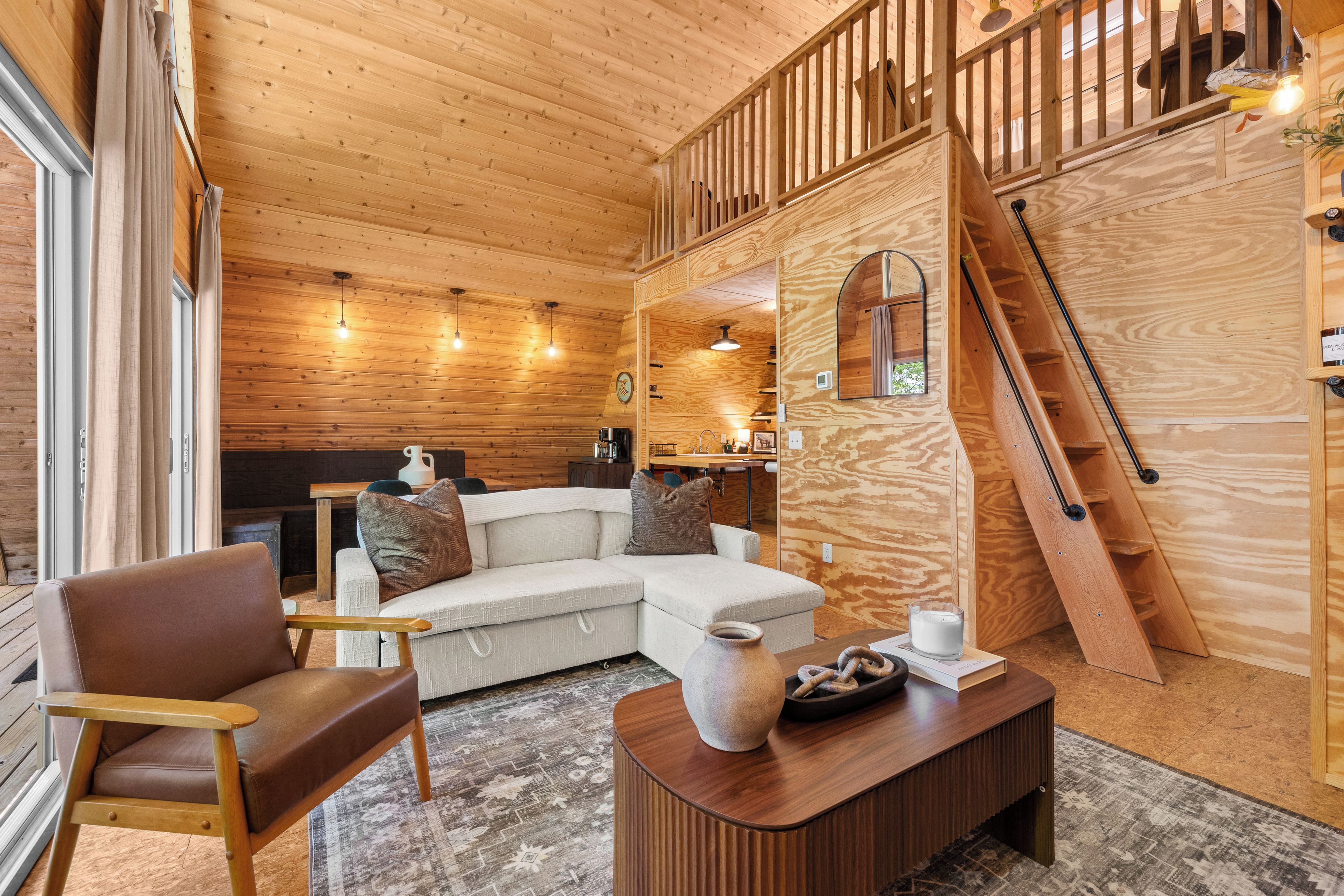 Interior acollidor d'una cabana amb elements de fusta, un sofà, una taula de centre i una escala.