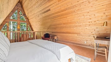 Ein Schlafzimmer mit einem großen Bett, einem Schreibtisch und einem Sessel, mit Holzwänden und einer geneigten Decke.