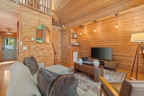 A cozy wooden interior with a sofa, television, and a staircase leading to an upper level.
