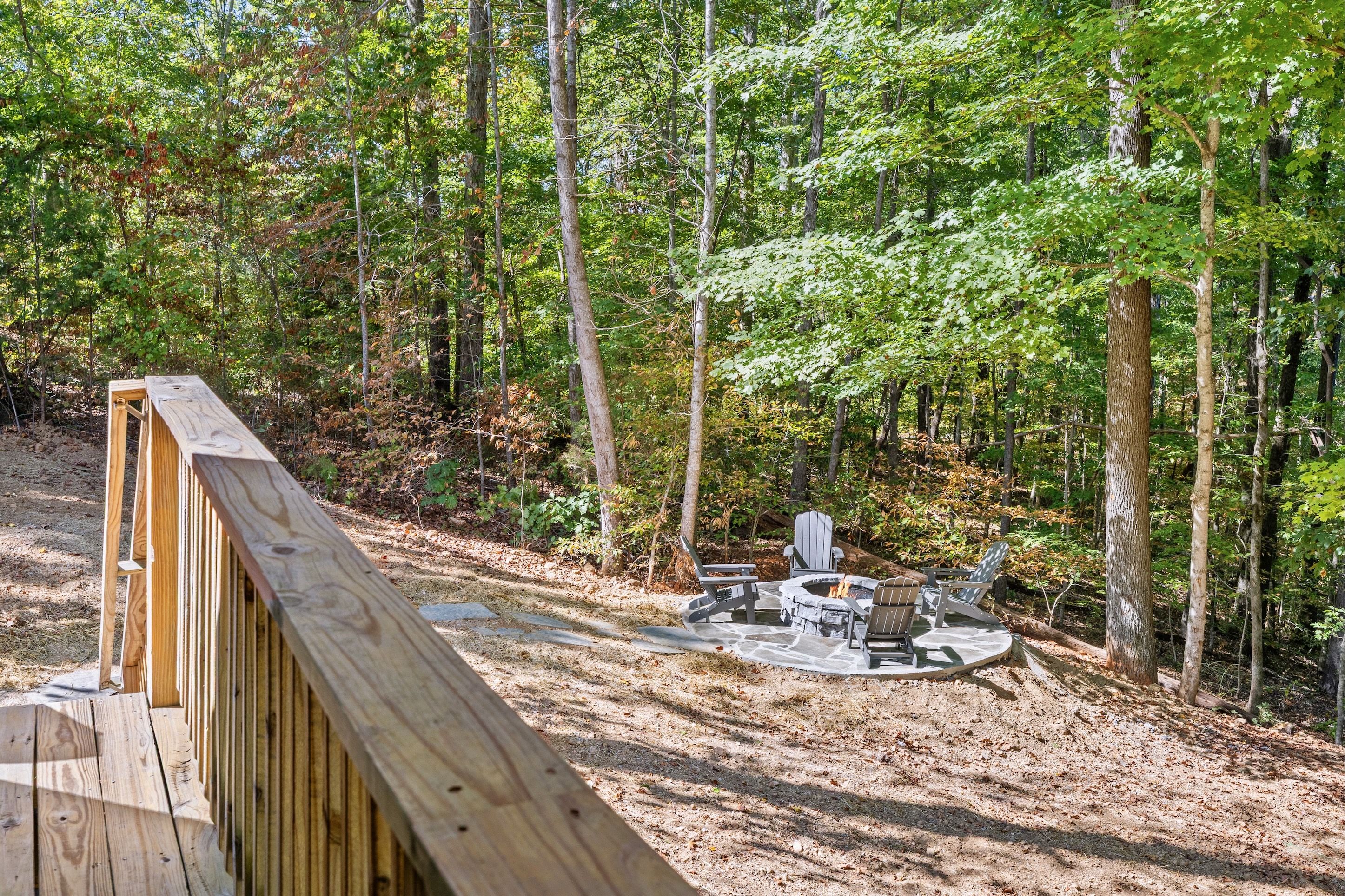Una terraza de madera con un hogar a piedra y sillones Adirondack en un área boscosa.