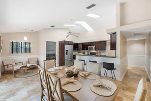 A spacious dining area with a wooden table set for four, surrounded by chairs. A ceiling fan and recessed lighting are visible above. - Heated Pool - 3BR Home in Marco Island - EV Charging (Marco Island)