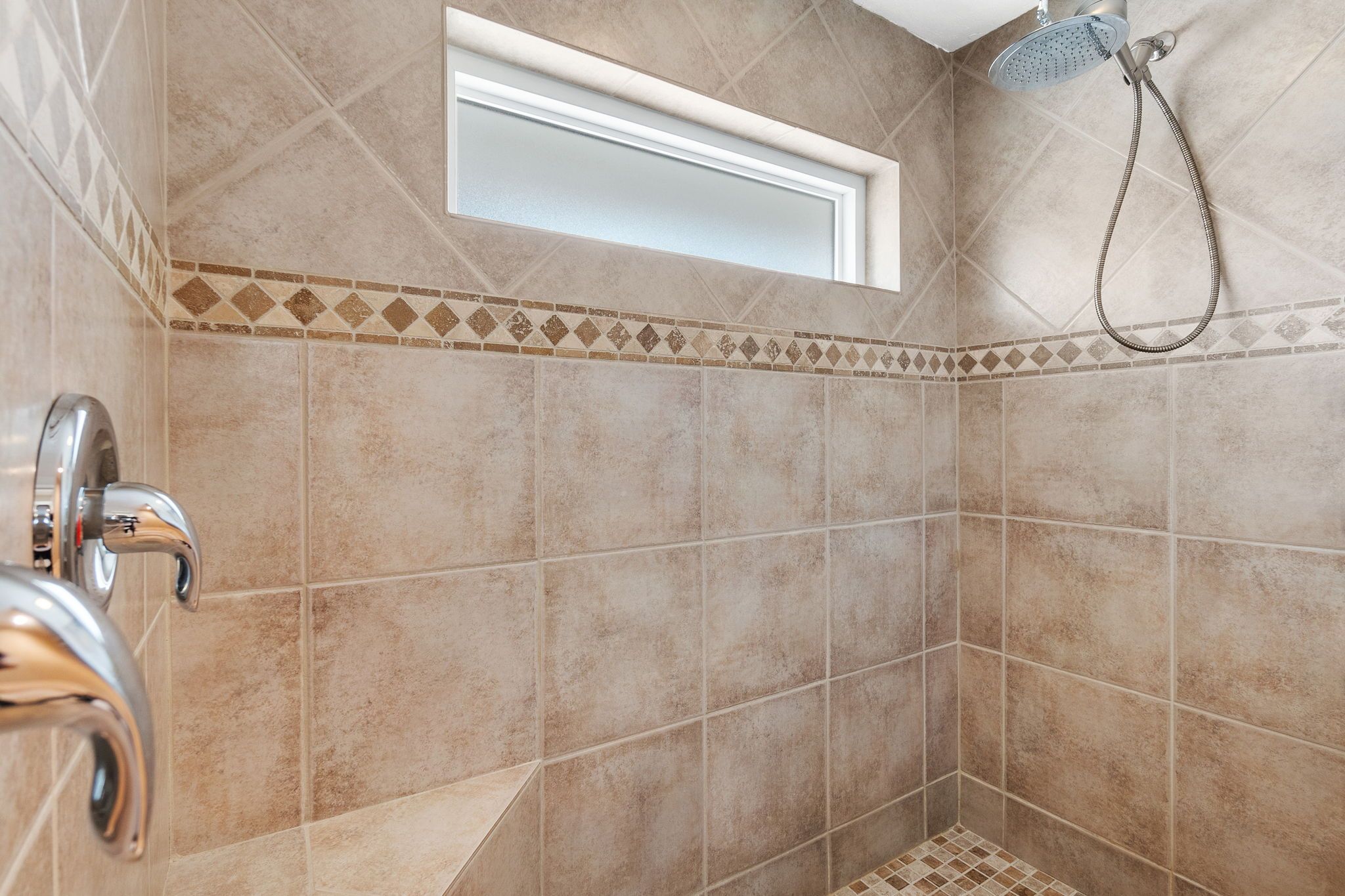 Un baño con azulejos color beige, un cabezal de ducha y un lavamanos en esquina.