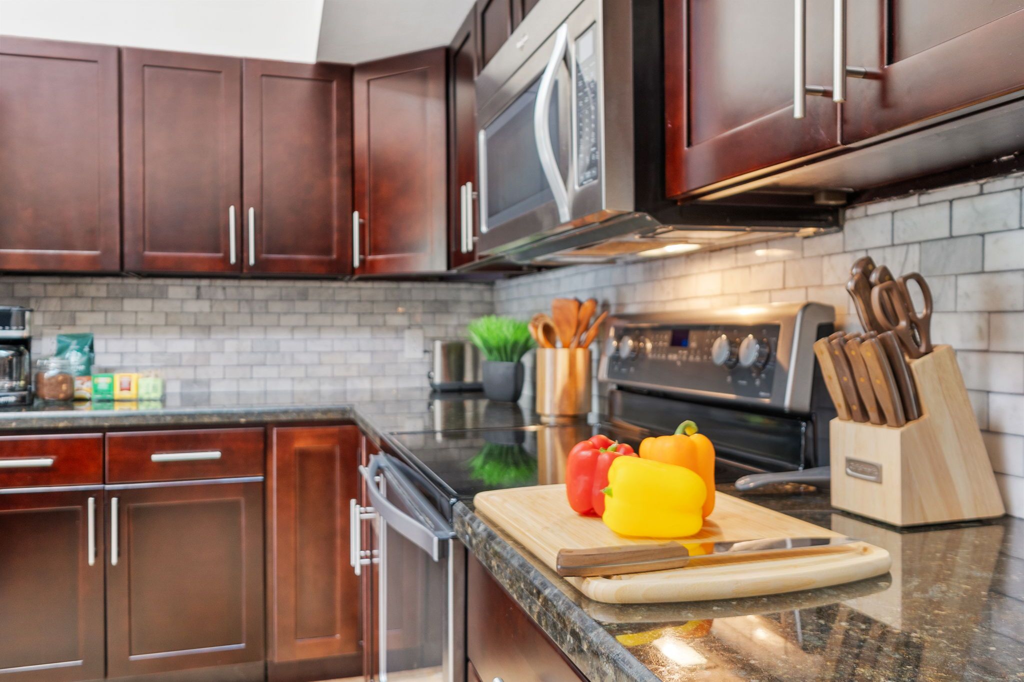 A modern kitchen with dark wooden cabinets, a stainless steel microwave, and a granite countertop.