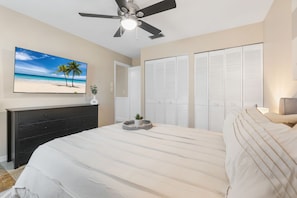 Un dormitorio con cama, ventilador de techo, un cuadro de playa, cómoda y armario.