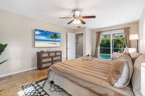 A bedroom with a bed, a ceiling fan, a painting of a beach, a wooden cabinet, and a view of a pool through a glass door. - Heated Pool - 3BR Home in Marco Island - EV Charging (Marco Island)