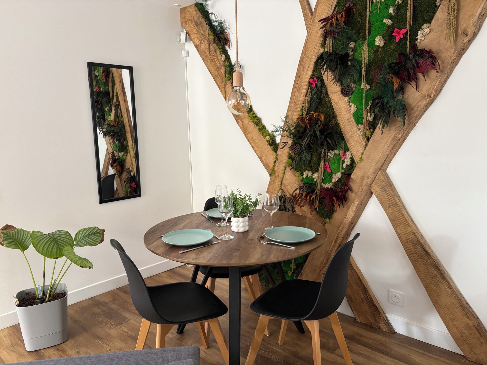 A dining area with a round wooden table, black chairs, and a wall-mounted plant.