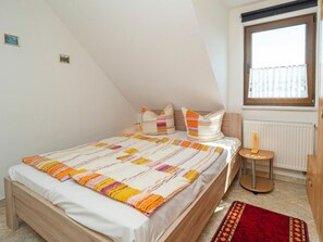 Ein Schlafzimmer mit einem Bett, einem Fenster, einer Heizung und einem kleinen Tisch mit einer Flasche.